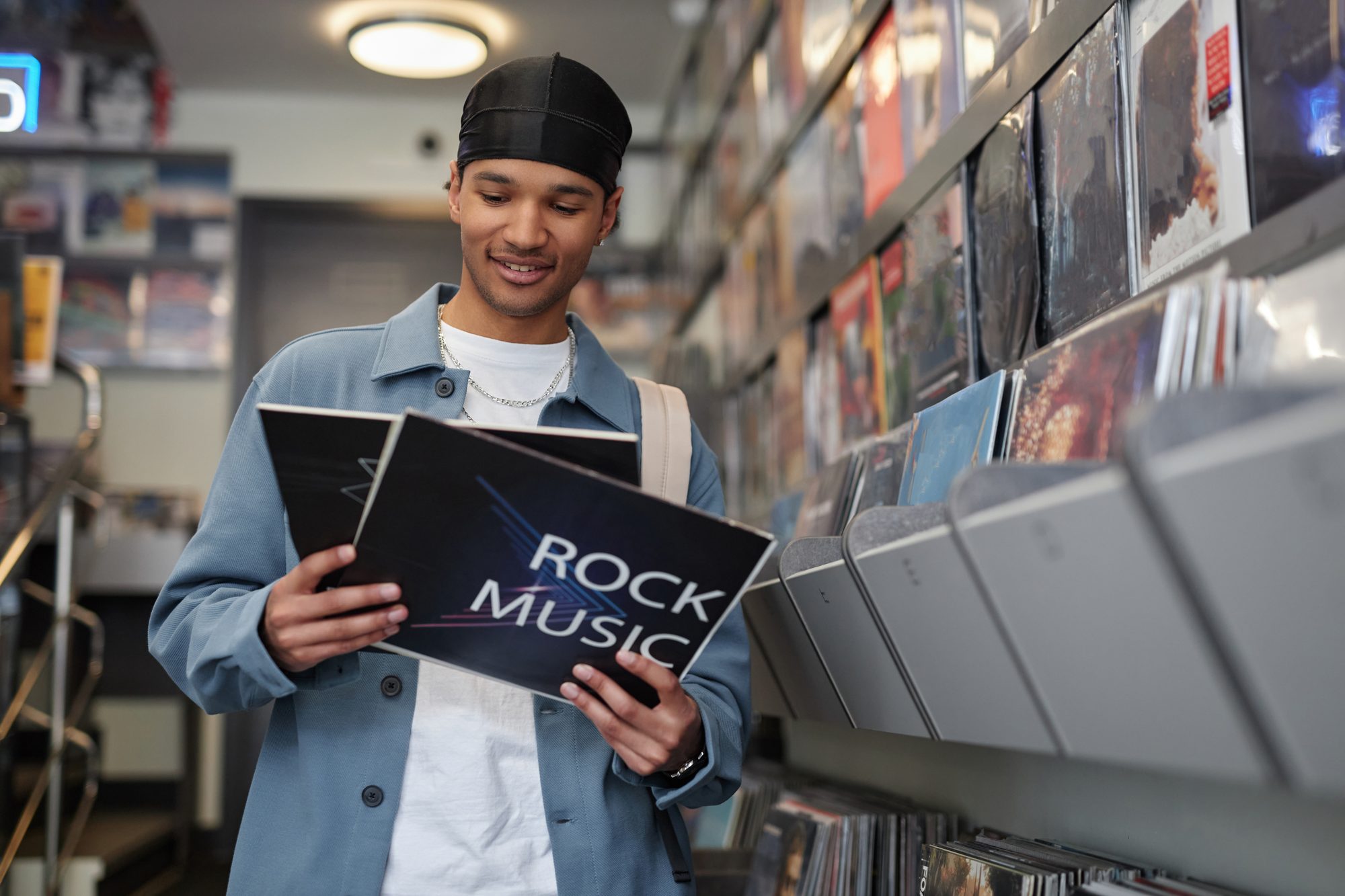 Smiling man holding a rock vinyl record sleeve in a record store